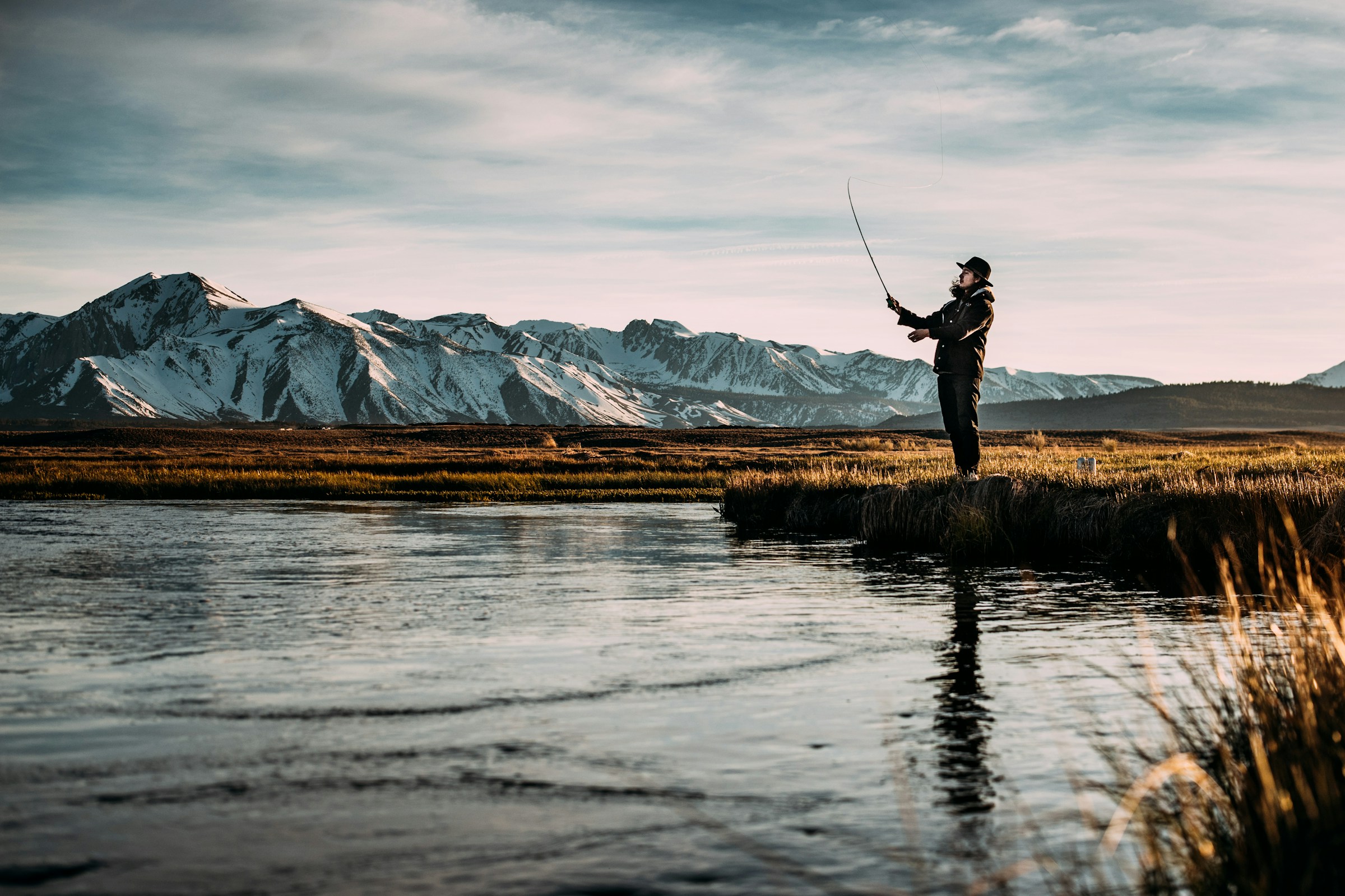 Fly angler wading a river at dusk with mountains behind